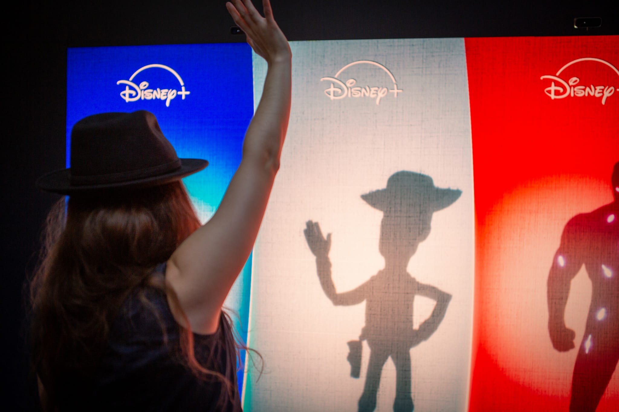 Visitor waving at Woody's shadow on the interactive Disney+ shadow wall