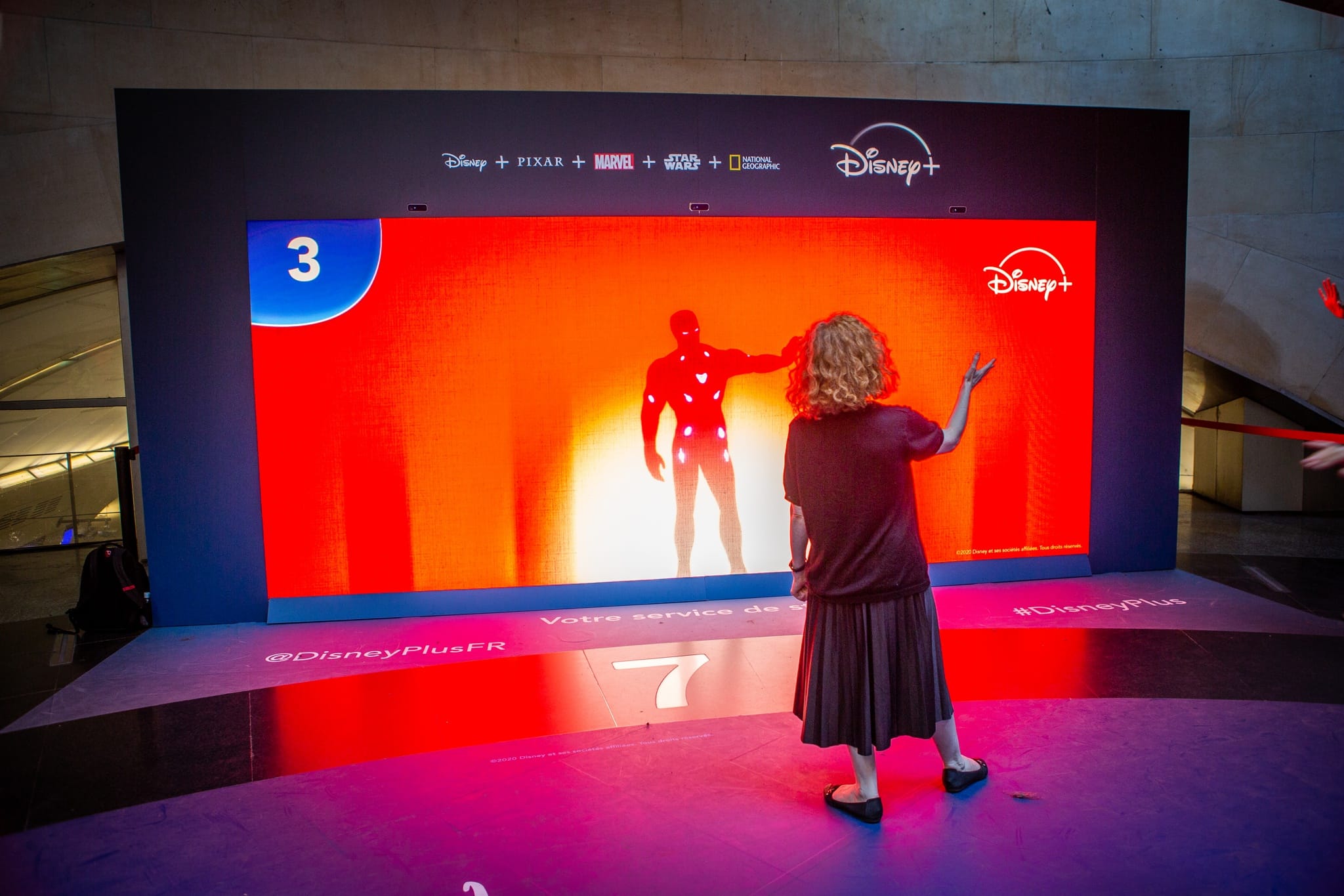 Visitor facing Iron Man's shadow on the Disney+ wall of shadows