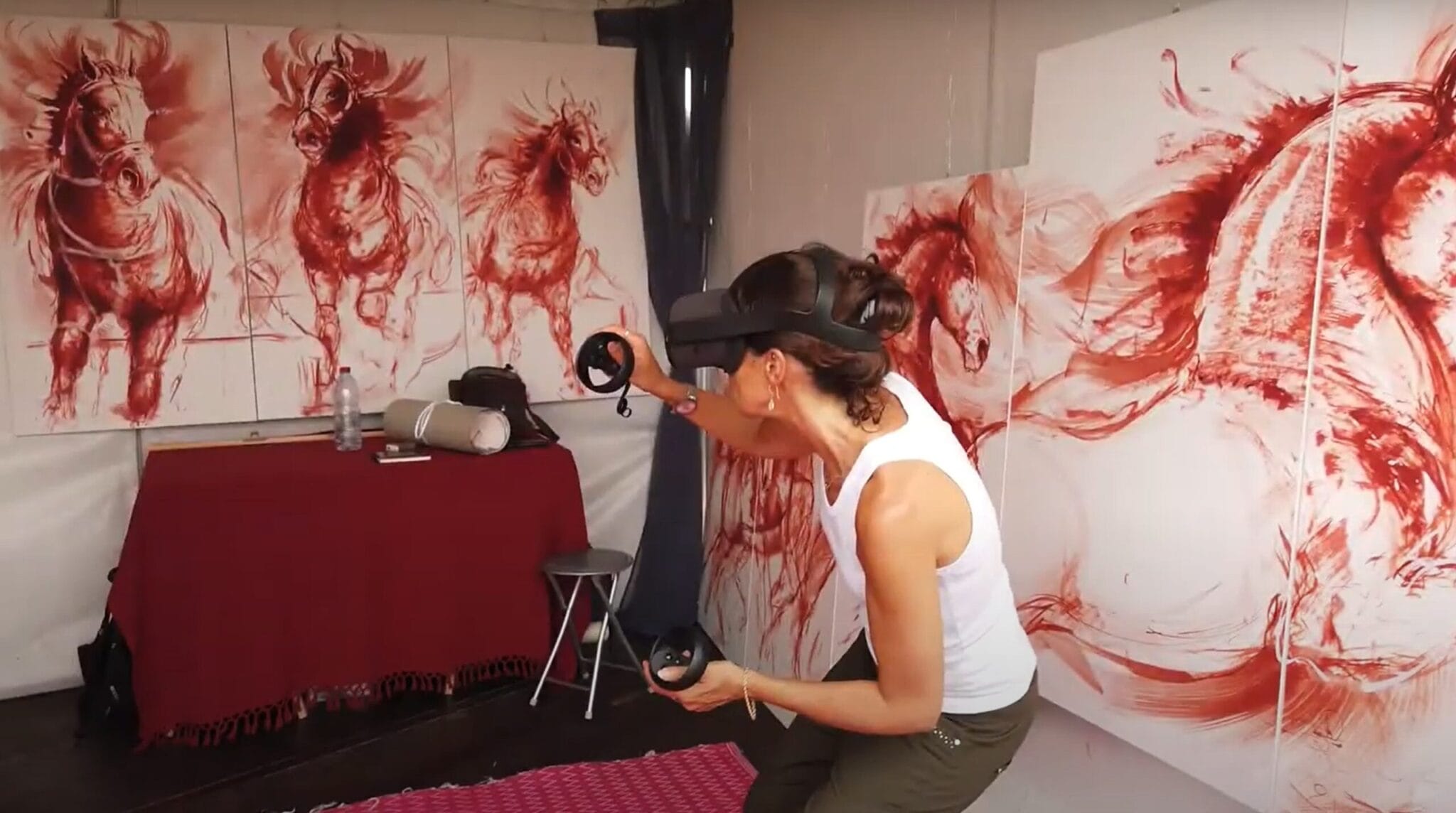 Artist in a VR headset painting in 3D in front of red horse canvases, Anima Fer Chan project