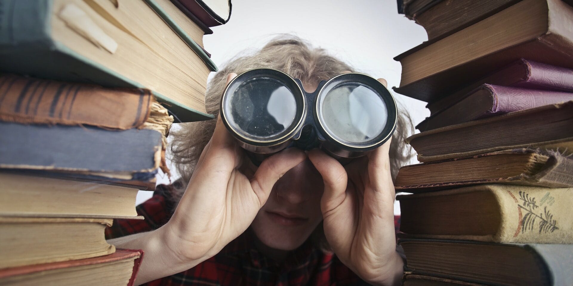 Person looking through binoculars between stacks of books
