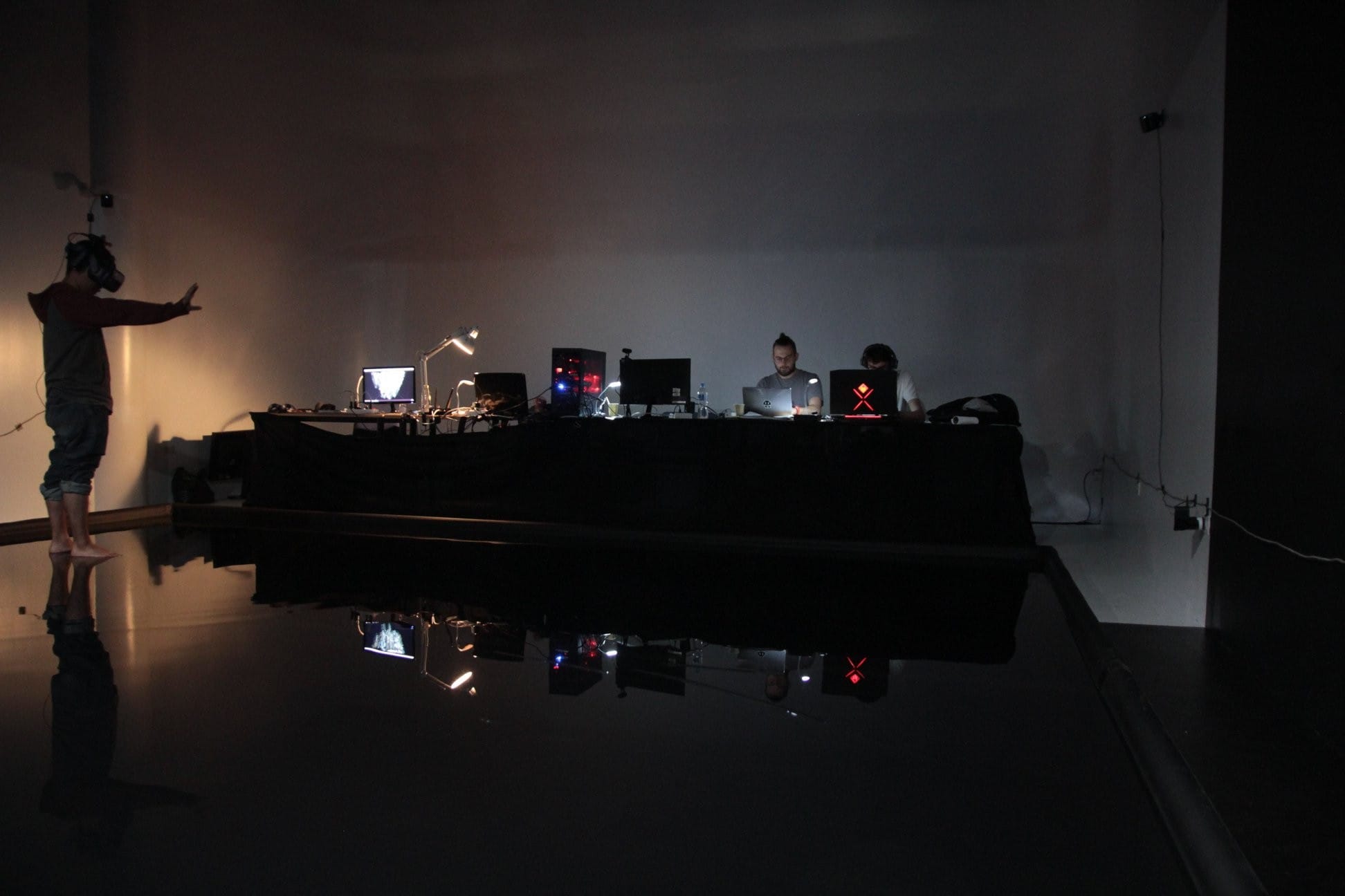 Performer in a VR headset facing a control desk in a dark room, "Encounters" work