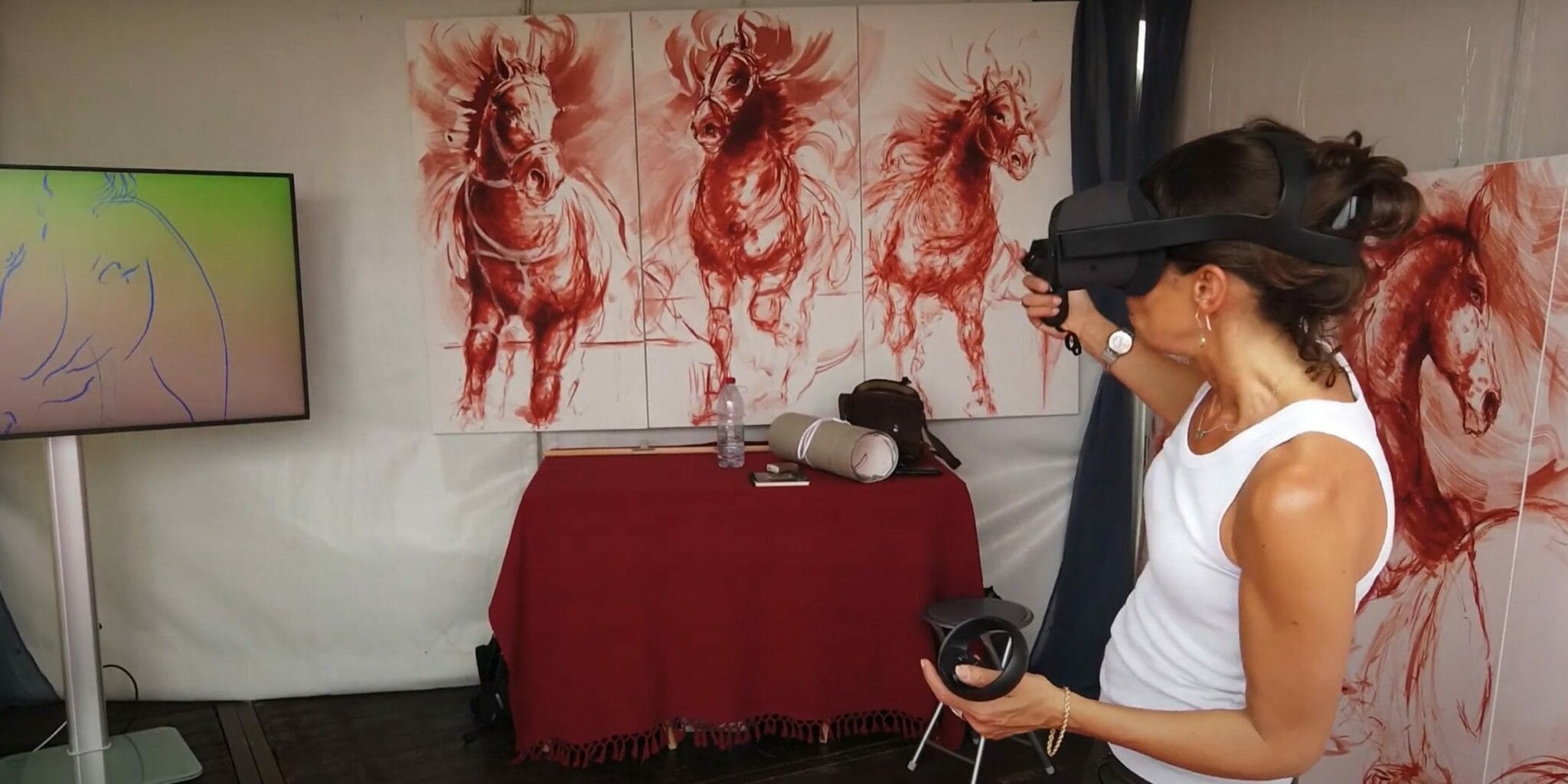 Artist in a VR headset painting in front of red horse canvases, Anima Fer Chan exhibition