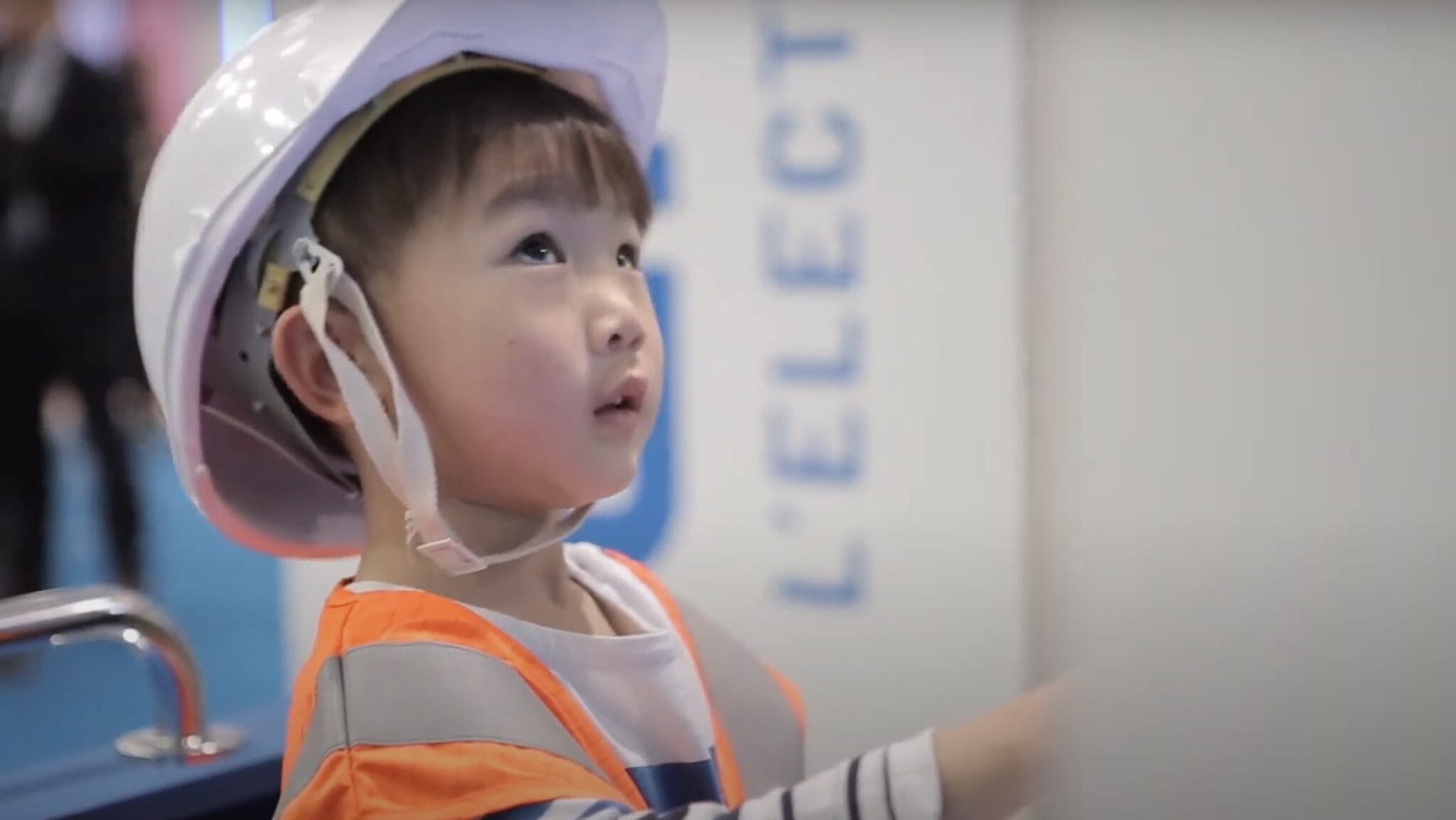 Child in a hard hat and orange vest watching the Enedis quiz screen